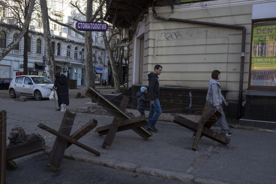 A family walks next to anti- tank barricades in Odesa, southern Ukraine, on Tuesday, March 22, 2022.(AP Photo/Petros Giannakouris)