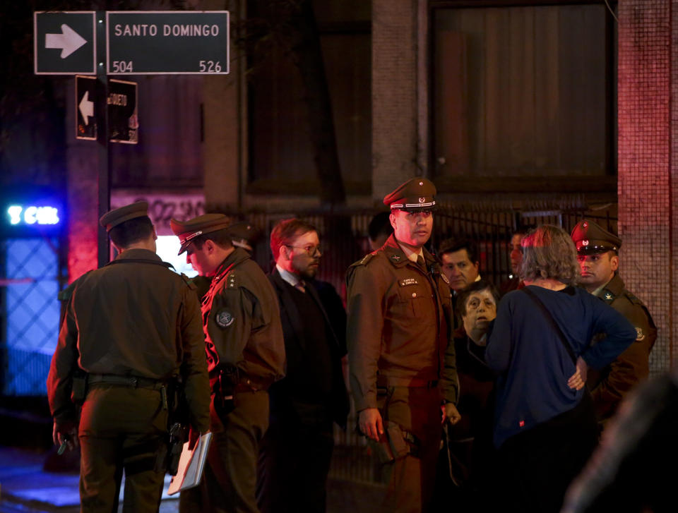 Chilean police talk with neighbors in front a building where six Brazilians died of apparent carbon monoxide poisoning at an old apartment in Santiago, Chile, Wednesday, May 22, 2019. Police commander Rodrigo Soto said officers found four adults and two children dead at the six-story building Wednesday. The fire department said a high concentration of carbon monoxide was measured in the apartment, which it said was completely closed. (AP Photo/Esteban Felix)