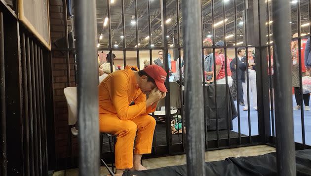 CPAC attendees look at a bizarre exhibit in which an actor, pretending to be a Jan. 6 rioter, sobs in a jail cell. (Photo: Laura Jedeed)