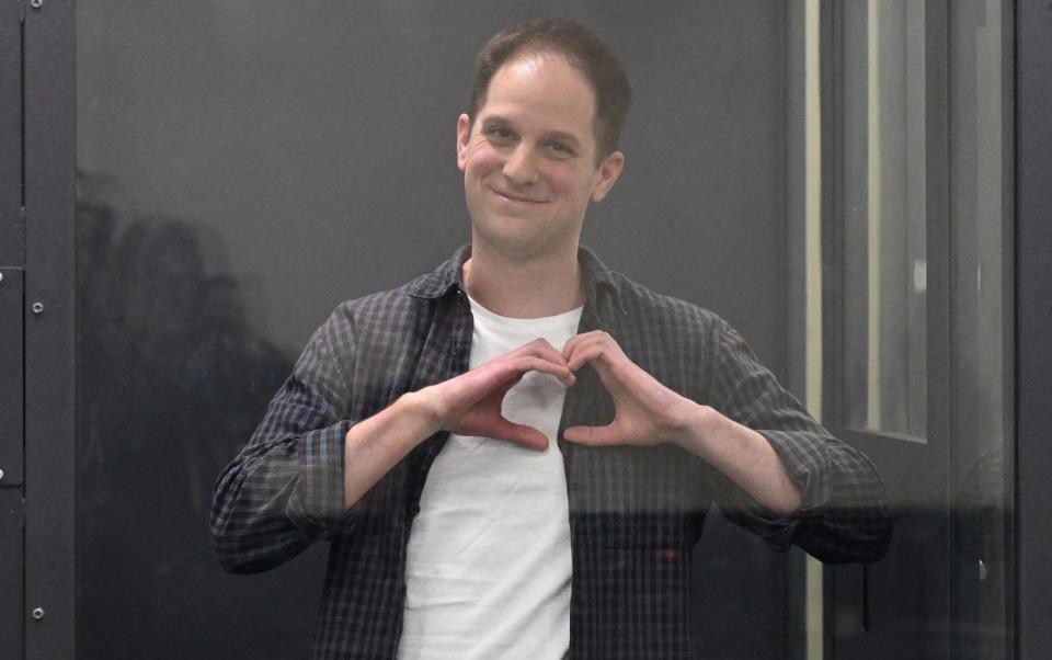 Mr Gershkovich makes a heart gesture with both hands held to his chest, from behind glass in court