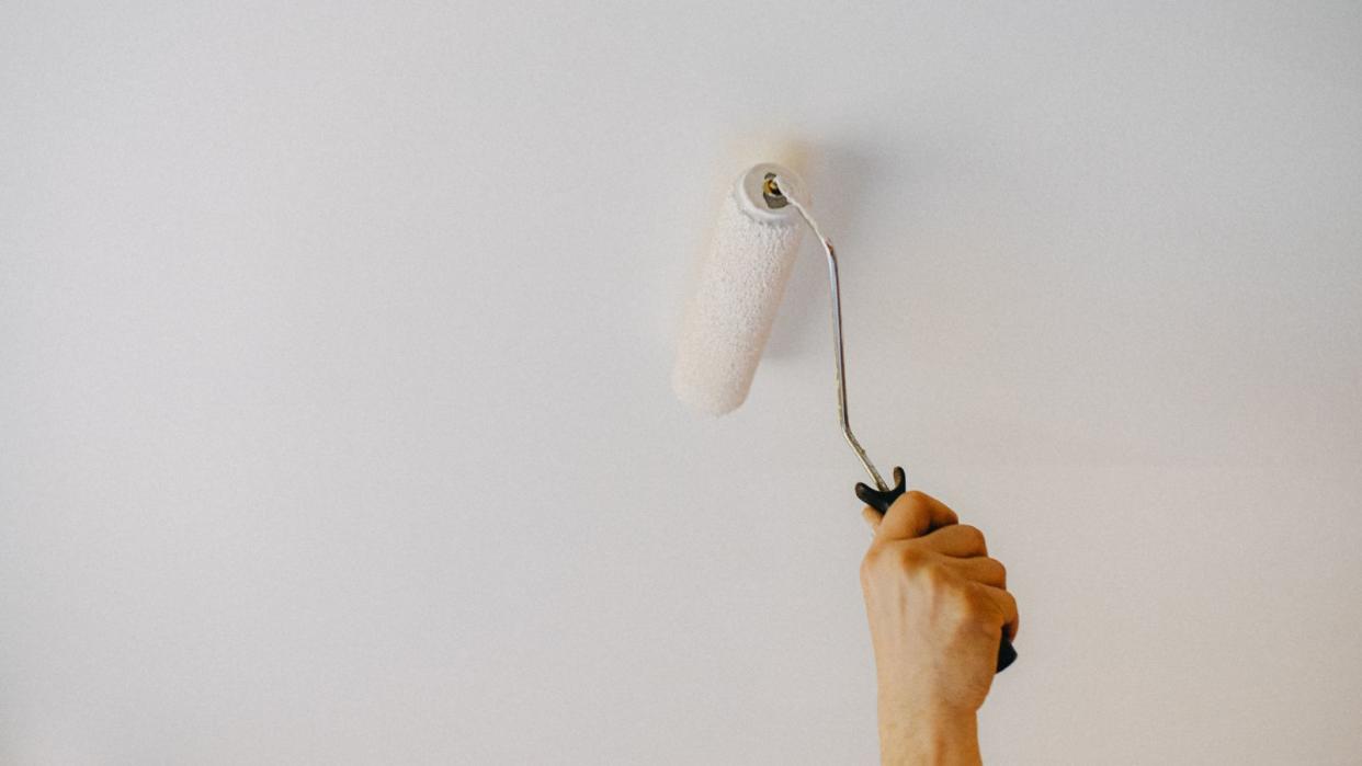  Soeone using a white roller to paint a ceiling  