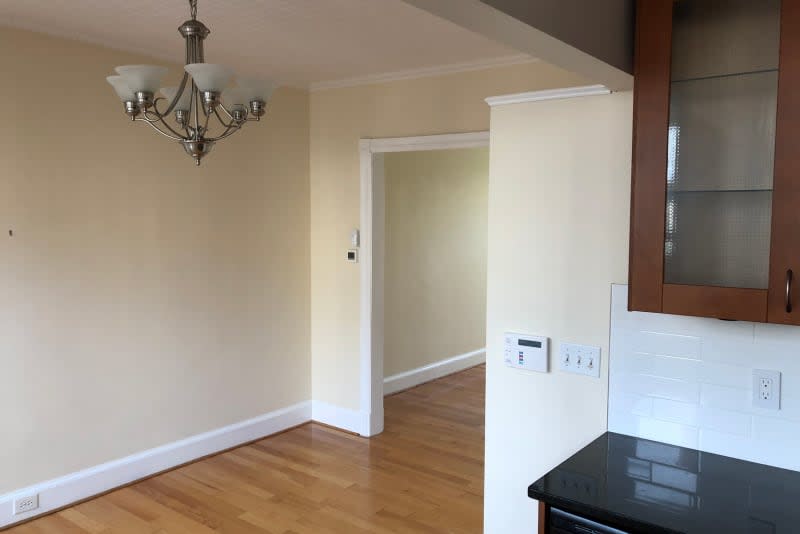 Bare dining room with hanging light fixture and corner of kitchen cabinets