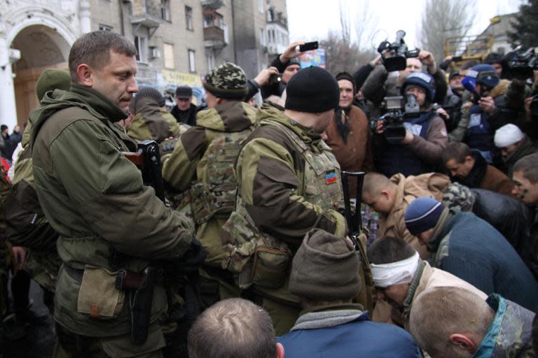 Captive Ukrainian soldiers kneel as the leader of the self-declared Donetsk People's Republic, Alexander Zakharchenko (L), stands at a bus stop where 13 people were killed in a trolleybus shelling in Donetsk, on January 22, 2015