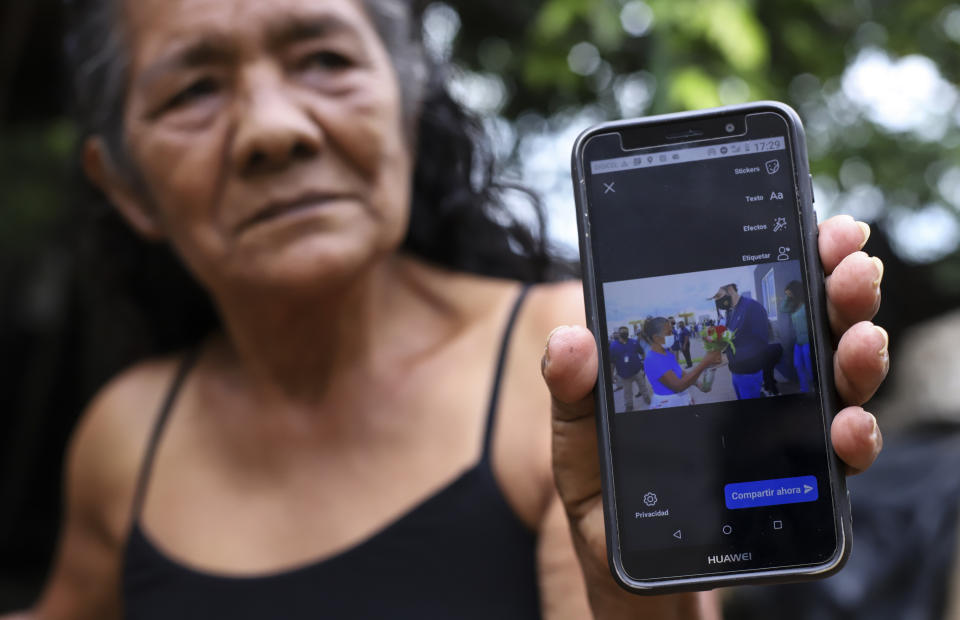 Ines Flamenco holds up her smartphone showing a December 2020 photo of her presenting President Nayib Bukele with a bouquet of flowers, during an interview on her farm in Los Angelitos, El Salvador, Wednesday, July 28, 2021. Flamenco is one of a group of landslide survivors who have returned the homes given to them by the government. She said that if she had accepted she would been forced to abandon her farm animals. "They took me to a place without asking and then accused me of being ungrateful for a gift that I didn't ask for." (AP Photo/Salvador Melendez)