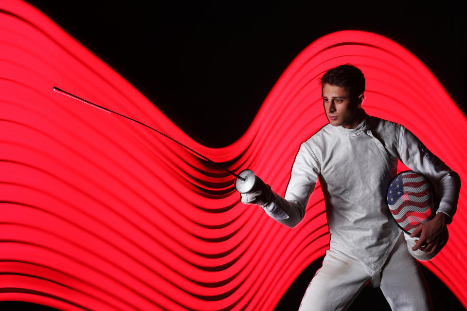 Nick Itkin in fencing equipment, foil extended, with red strobing background.