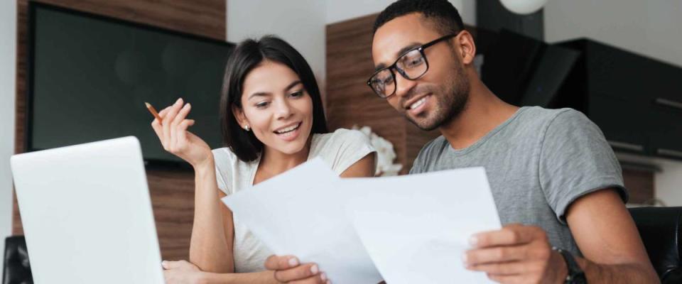 Photo of cheerful young couple using laptop and analyzing their finances with documents.