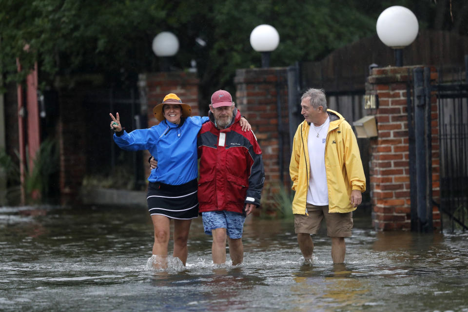 Isabelle Schneidau, left, gestures to the camera as she walks in a rising storm surge with Mont Echols, center, and L.G. Sullivan, right, after checking on their boats in the West End section of New Orleans in advance of Tropical Storm Cristobal in New Orleans, Sunday, June 7, 2020. (AP Photo/Gerald Herbert)