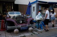 A pandemic prevention worker sits next to a vintage car as he scans a man's ID card at a nucleic acid testing station, amid a coronavirus disease (COVID-19) outbreak, in Beijing