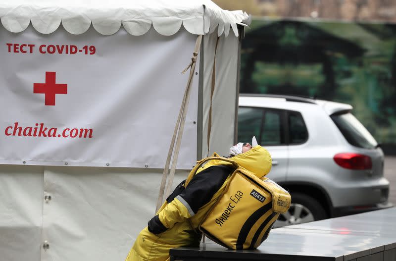 A Yandex.Eats food delivery courier rests near a mobile laboratory in Moscow