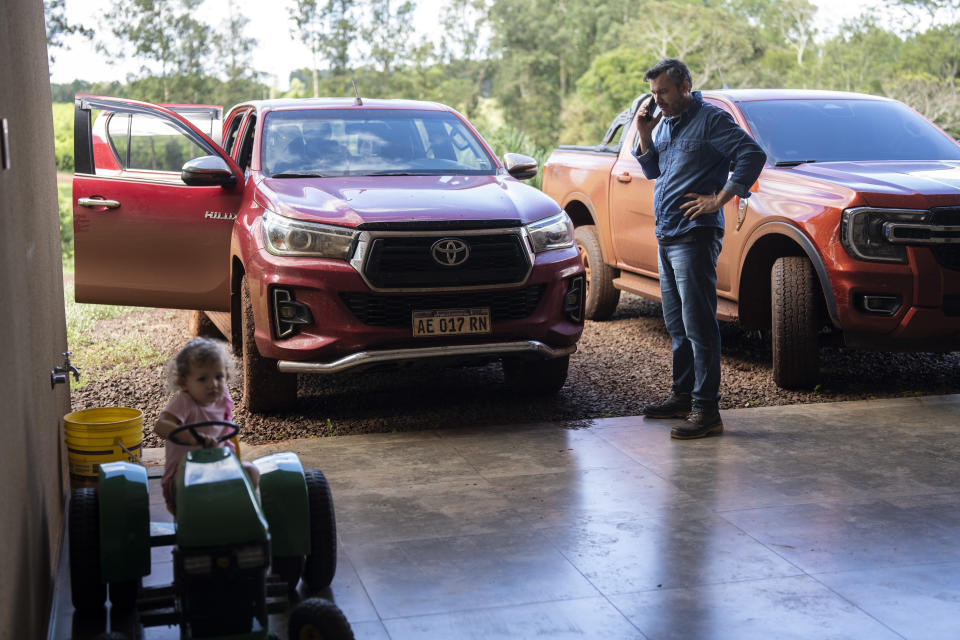 El productor de yerba mate Julio Petterson recibe una llamada de trabajo en su casa, donde su hija Kiara Isabella juega con un tractor de juguete en Andresito, en la provincia argentina de Misiones, el miércoles 17 de abril de 2024. "Apenas sobrevivimos", dijo Petterson, aludiendo a las políticas que devastaron la industria de la yerba mate en la década de 1990. (AP Foto/Rodrigo Abd)