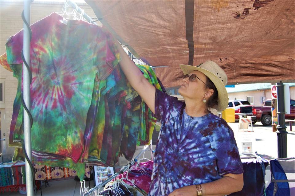 Artist Danni Andrew adjusts a rack of tie-dye T-shirts at her tent at the first Makers Market of the season June 2 in Orchard Plaza in downtown Farmington.