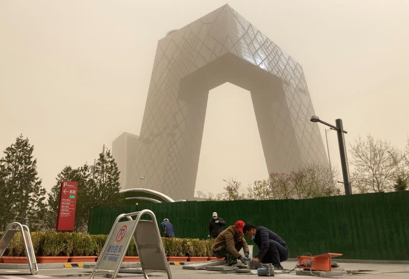 Construction workers are seen in front of the CCTV headquarters shrouded in dust as the city is hit by a sandstorm, in Beijing