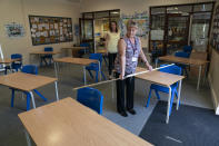 Year 6 teacher Jane Cooper uses a 2 meter length of ruler and pipe to check seat spacings in her classroom as measures are taken to prevent the transmission of coronavirus before the possible reopening of Lostock Hall Primary school in Poynton near Manchester, England, Wednesday May 20, 2020. (AP Photo/Jon Super)