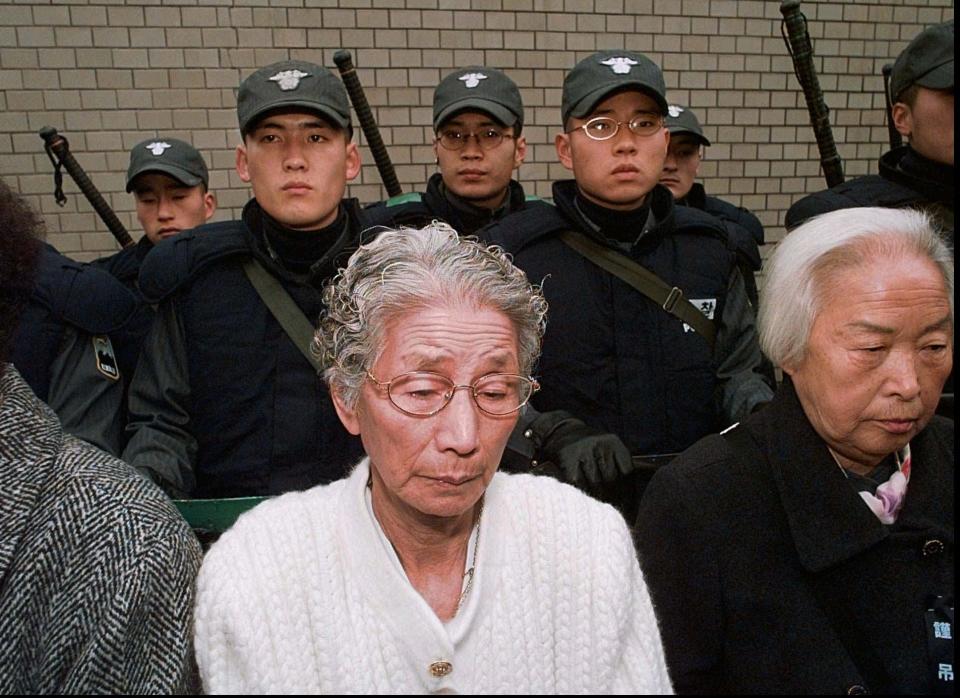 Against a backdrop of Seoul riot policemen in front of the Japanese embassy former "comfort women" bow their heads in silence as prayers are read for Kim Hak-soon Thursday, Dec. 18, 1997. Kim, who died Tuesday was the first to openly identify herself as a former sex slave of Japanese soldiers during World War II. (AP Photo/David Longstreath)