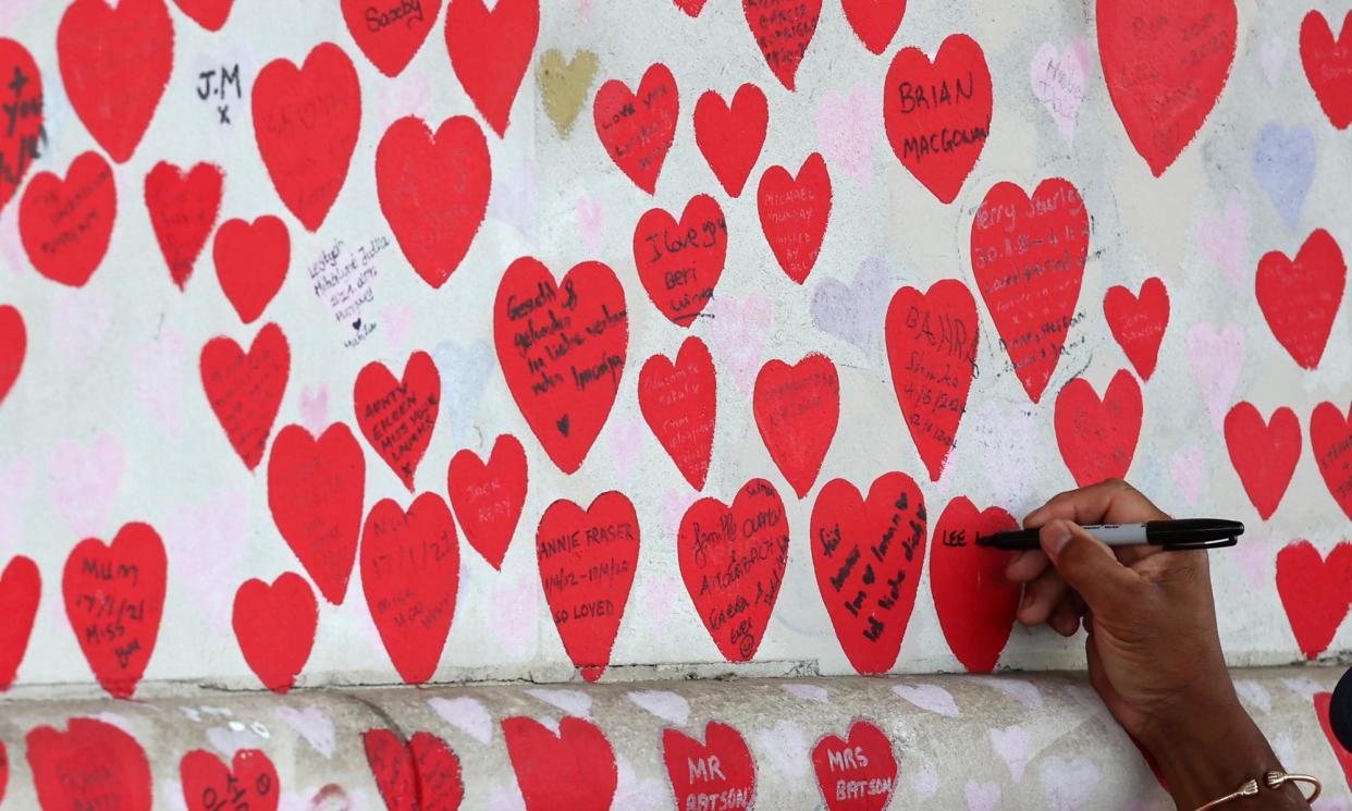 <span>People pay tribute to loved ones at the Covid memorial wall in London.</span><span>Photograph: Toby Melville/Reuters</span>