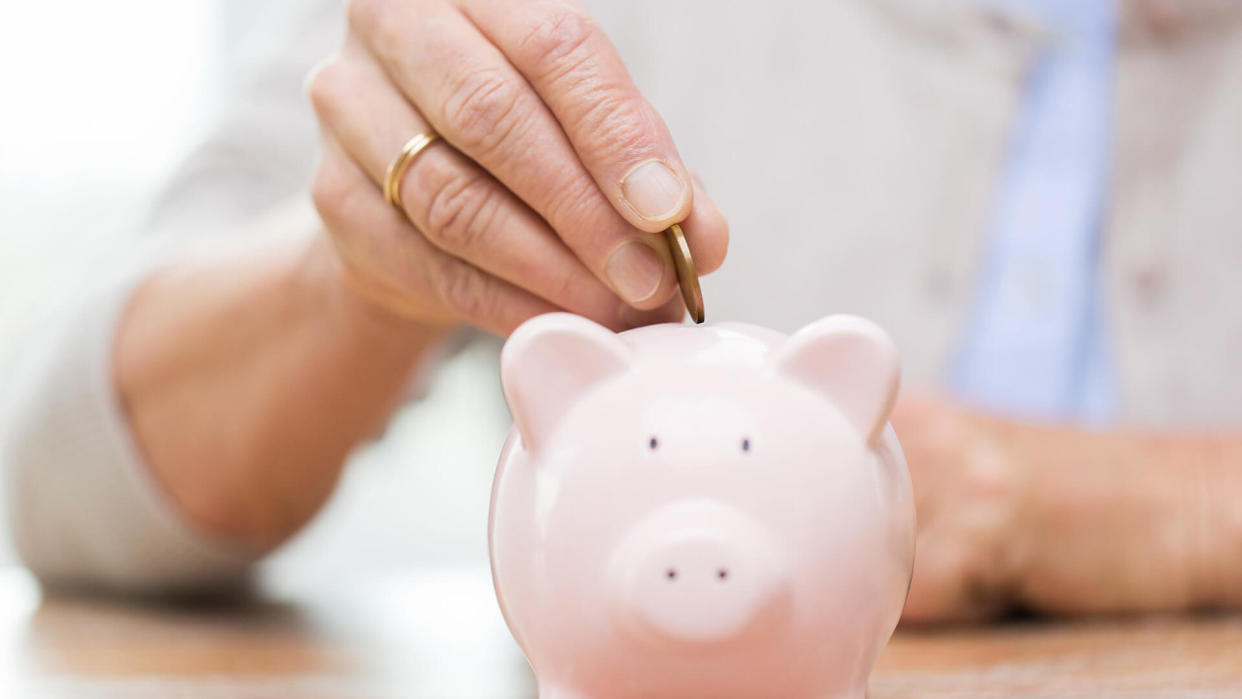 senior woman putting coin into piggy bank.