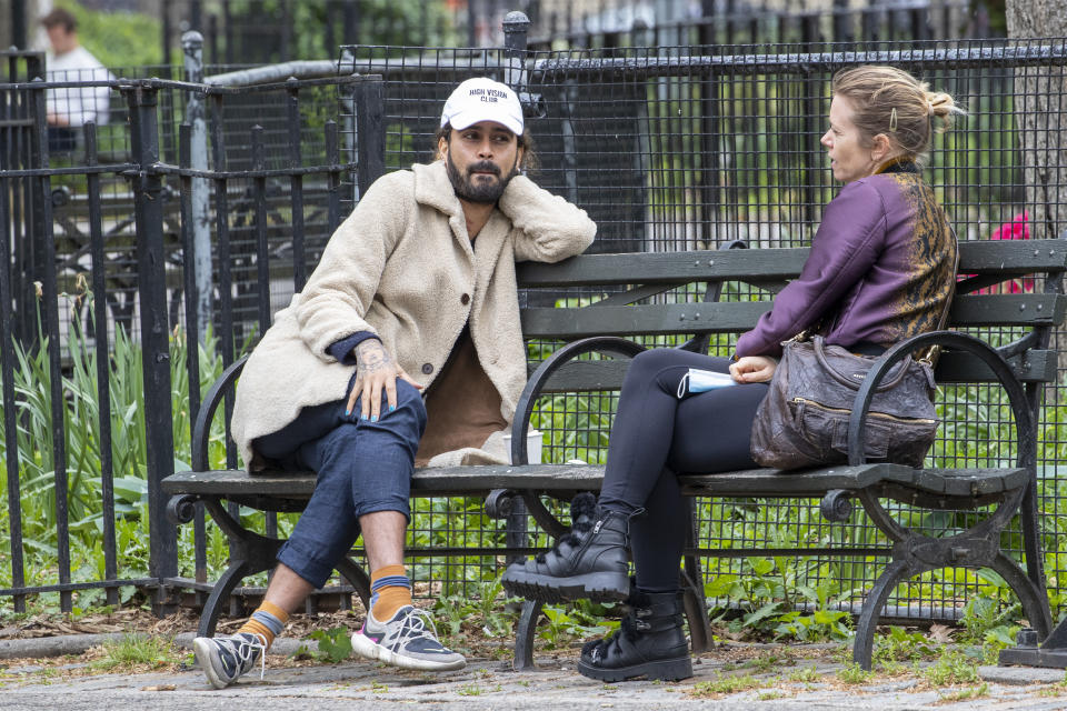 In this Monday, May 11, 2020 photo, a couple, not wearing face masks, sit at a distance from each other on a park bench in Tompkins Square Park in New York. New York's governor has ordered masks for anyone out in public who can't stay at least six feet away from other people. Yet, while the rule is clear, New Yorkers have adopted their own interpretation of exactly when masks are required, especially outdoors. (AP Photo/Mary Altaffer)