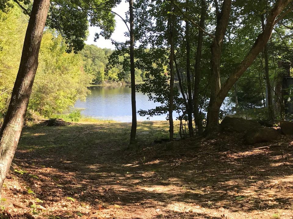 A tree-lined walkway leads to a beach on the shore of the Sprague Upper Reservoir at the former YMCA Camp Shepard, now owned by the Town of Smithfield.