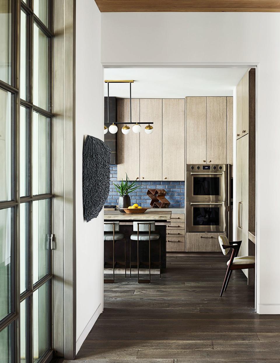 The kitchen features custom oak cabinetry, Wolf wall ovens, Tabarka Studio backsplash tile, and Arteriors lighting; the beaded artwork is by Paola Pivi.