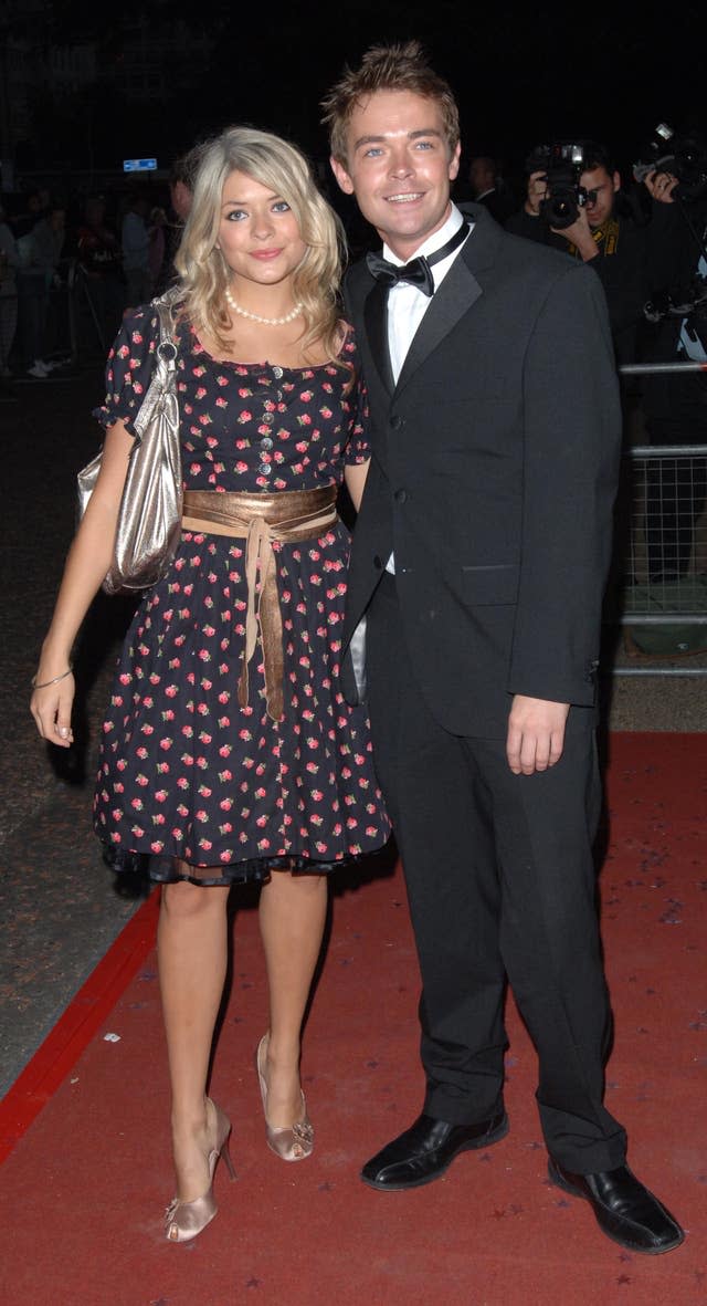 Holly Willoughby in a black dress arm-in-arm on a red carpet with Stephen Mulhern in a dress suit
