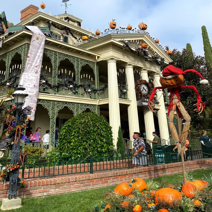 Outside the Haunted mansion dressed up with pumpkins, candles, a scarecrow wearing a santa suit, and a long list of gifts from the nightmare before christmas