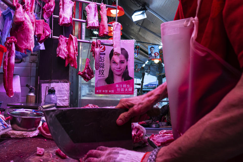 A butcher works as posters promoting candidates for upcoming district council elections stand in the background in Hong Kong, Tuesday, Nov. 28, 2023. (AP Photo/Louise Delmotte)