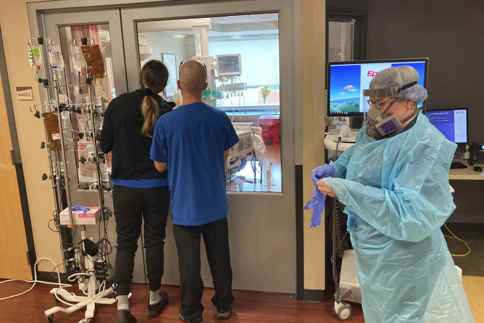 FILE - In this Aug. 20, 2021, file photo, two visitors peer into the room of a COVID-19 patient in the intensive care unit at Salem Hospital in Salem, Ore., as a nurse dons full protective gear before going into the room of another patient. Gov. Kate Brown announced Wednesday, Aug. 25, 2021, that the state has contracted with a medical staffing company to provide up to 500 health care workers to hospitals around the state to help respond to the surge in patients due to the delta variant. (AP Photo/Andrew Selsky, File)