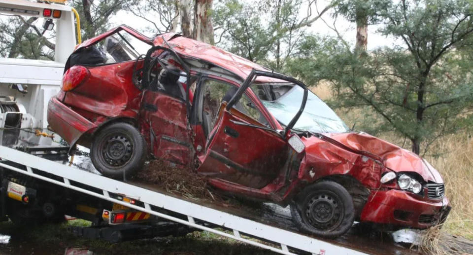 A wrecked red car can be seen on the back of a rescue truck.