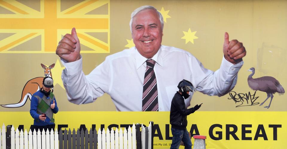 Two men in front of Clive Palmer billboard