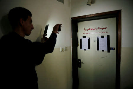 A Palestinian man uses his mobile phone to photograph a door of a Palestinian map office, covered with an Israeli police warrant and taped on the sides by Israeli security officers who carried out an Israeli police order to close the office, in the Arab East Jerusalem neighbourhood of Beit Hanina March 14, 2017. REUTERS/Ammar Awad