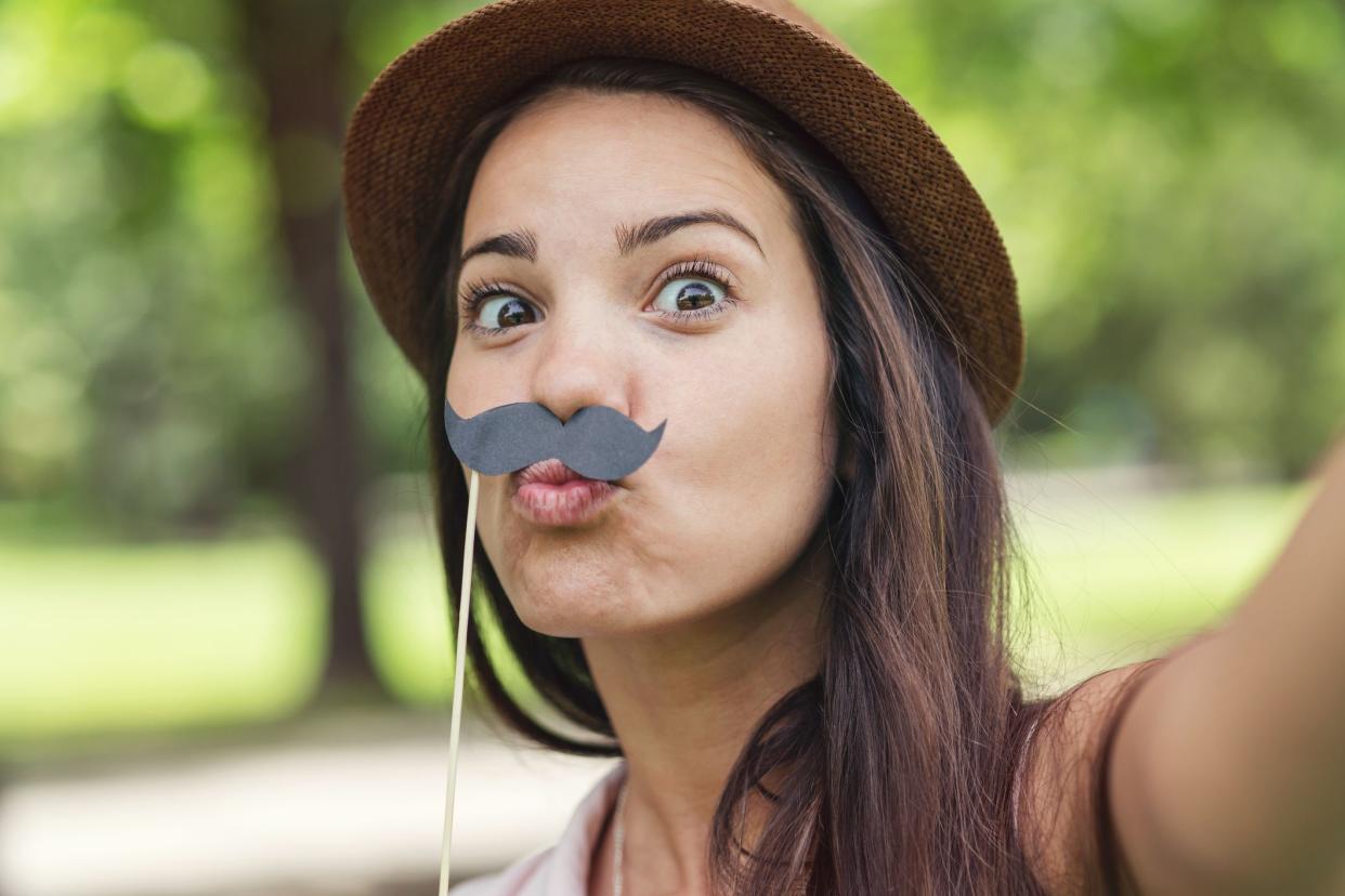 Girl making a selfie with fake moustaches and grimacing in the park