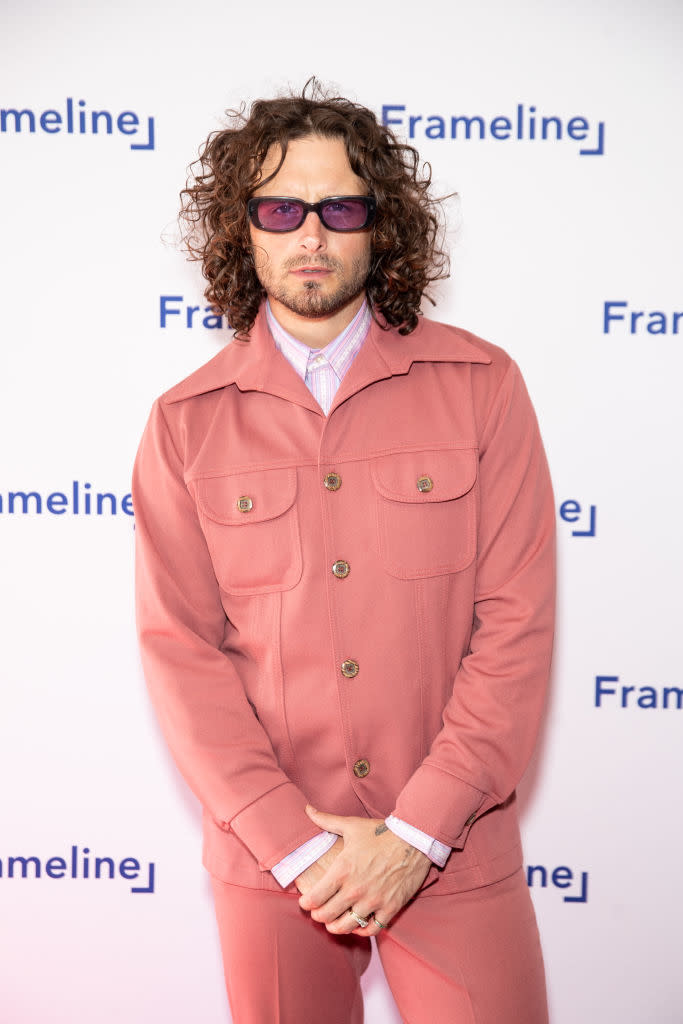 Nico in vintage-inspired suit with curly hair and sunglasses posing in front of a Frameline backdrop