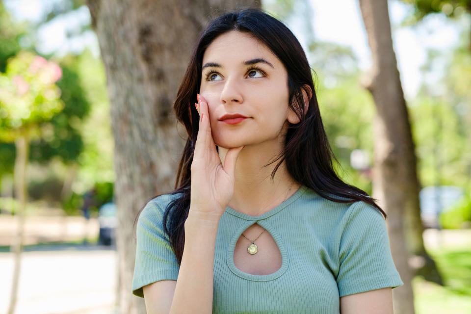 Woman in front of a tree and looking up while resting her hand on her face