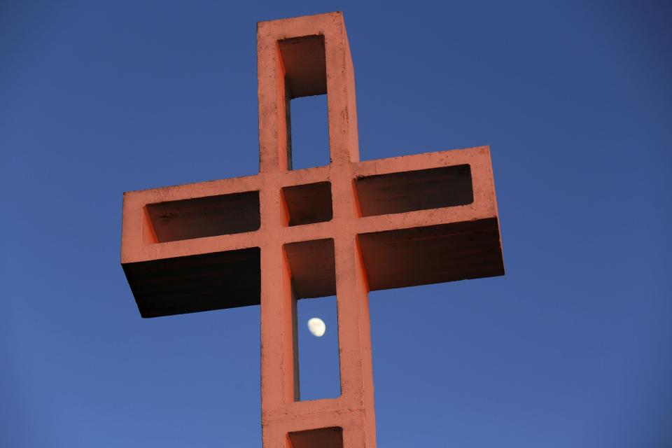 The moon is shown between the massive cross sitting atop the Mt. Soledad War Memorial in La Jolla
