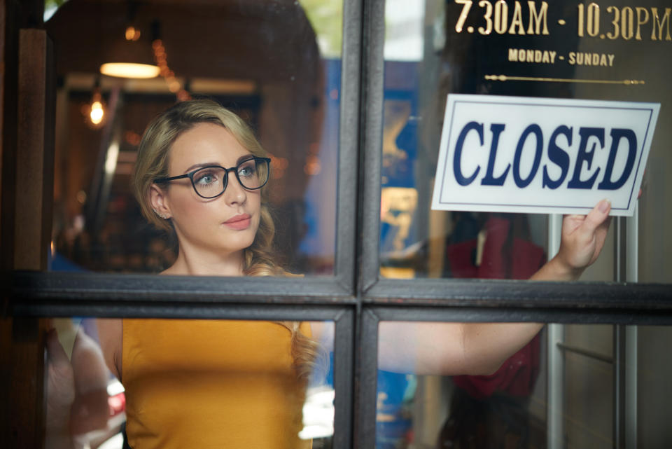 Woman holding a 'CLOSED' sign inside a door, looking outward