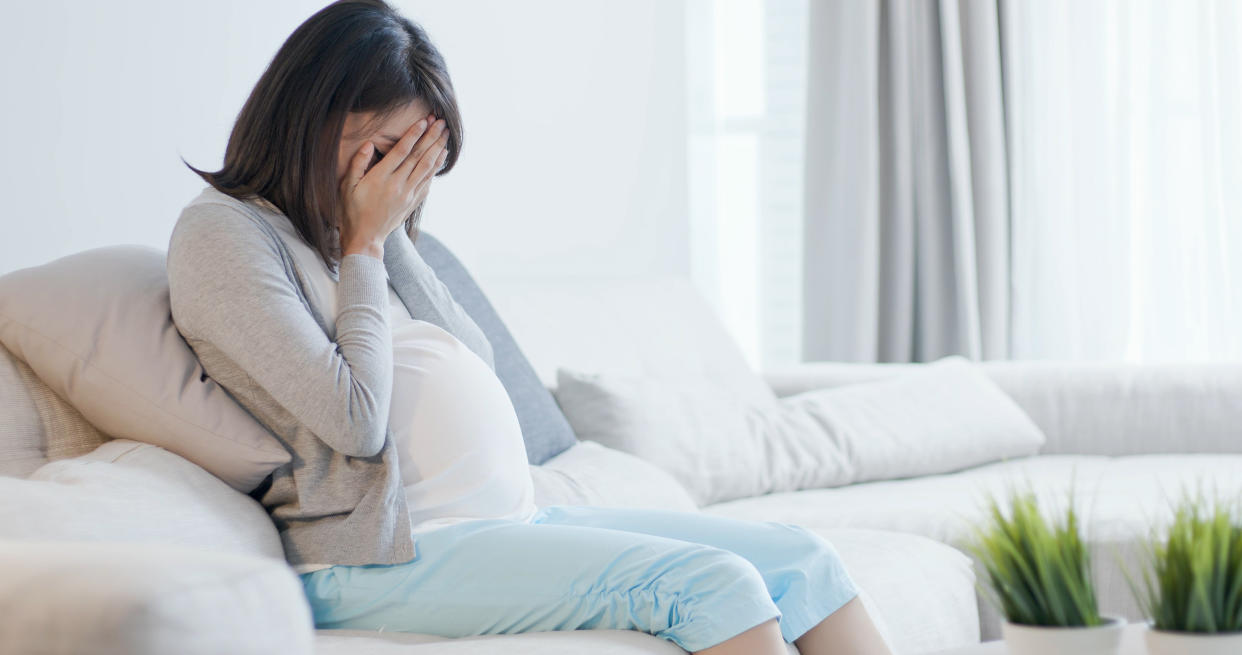 A pregnant woman sit on the sofa and feel depression at home. (Photo: Getty Images)