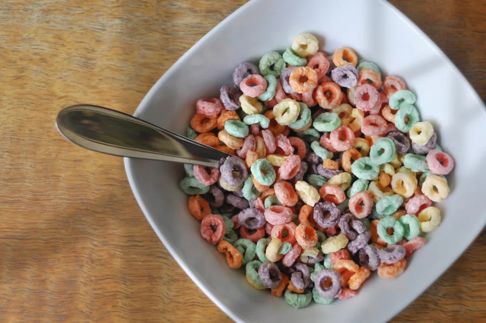 A bowl filled with colorful cereal rings and a spoon resting inside, placed on a wooden table