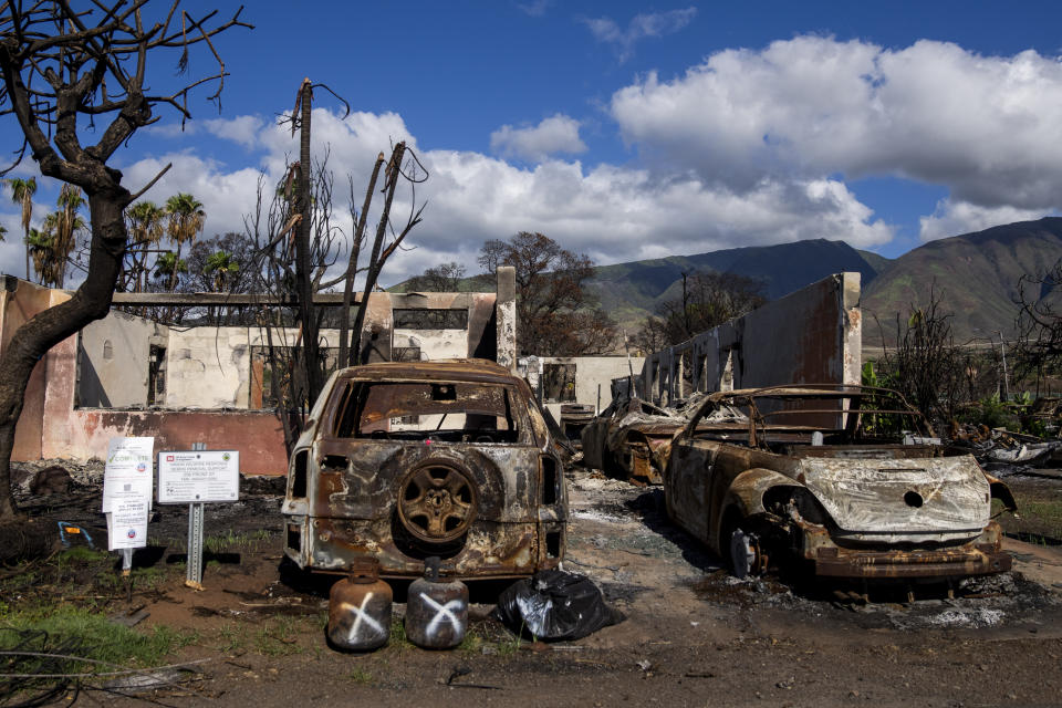 Burned cars and propane tanks with markings on them sit outside a house destroyed by wildfire, Friday, Dec. 8, 2023, in Lahaina, Hawaii. Recovery efforts continue after the August wildfire that swept through the Lahaina community on Hawaiian island of Maui, the deadliest U.S. wildfire in more than a century. (AP Photo/Lindsey Wasson)