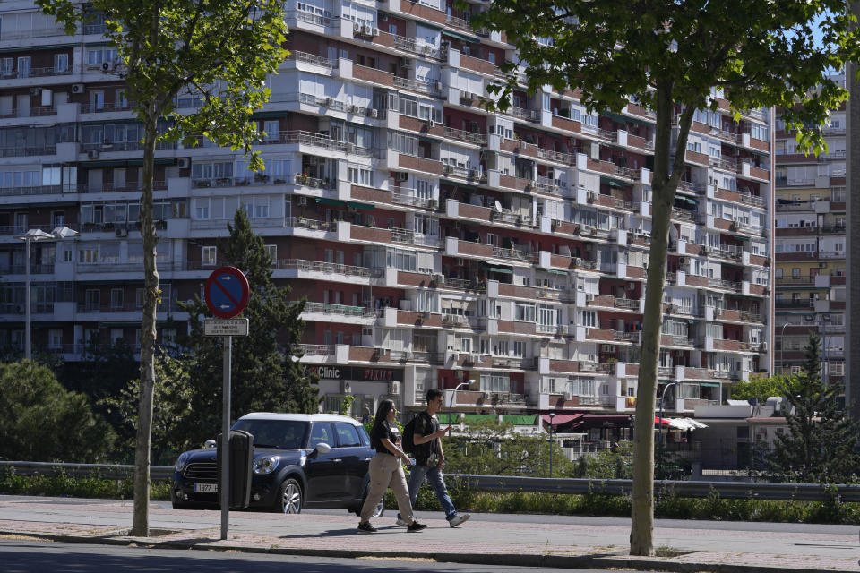 A young couple walk in front of housing blocks in Madrid, Spain, Tuesday, April 18, 2023. Spain's leftist coalition government has approved a plan to make available some 50,000 houses for rent at affordable prices as part of measures aimed at curbing soaring rents and house prices.The apartments will come from the state-controlled SAREB 'bad bank' that was set up in 2012 to relieve troubled banks of their most toxic assets during the international financial crisis. (AP Photo/Paul White)