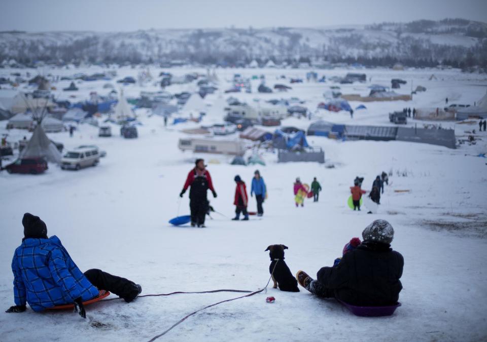 FILE - In this Thursday Dec. 1, 2016 file photo, the Oceti Sakowin camp where people have gathered to protest the Dakota Access oil pipeline stands in the background as a children sled down a hill in Cannon Ball, N.D. Some Native Americans worry the transition to a Donald Trump administration signals an end to eight years of sweeping Indian Country policy reforms. But Trump's Native American supporters said they're hopeful he will cut through some of the government red tape that they believe has stifled economic progress on reservations. (AP Photo/David Goldman, File)