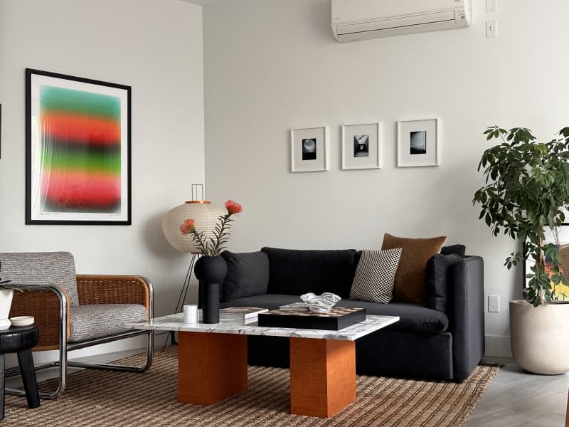 A woven chair next to a black fabric couch in a white living room.