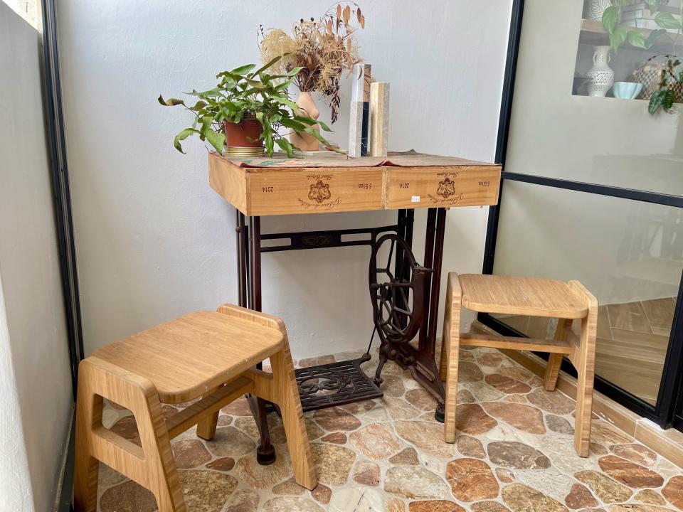 A small table made from a vintage sewing machine next to two small, wooden stools in their balcony area.