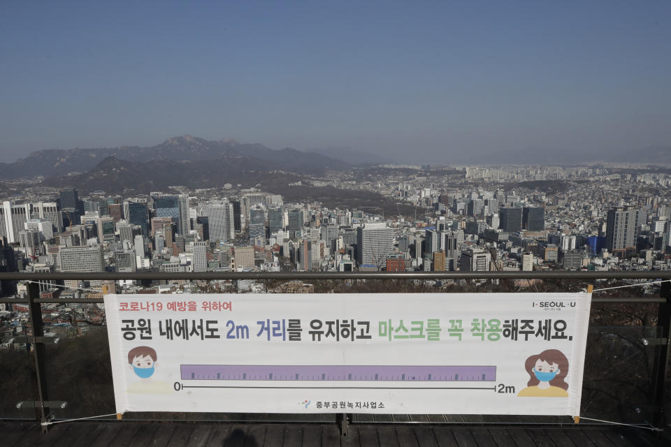 A banner showing a social distancing instruction is seen at a park, with a backdrop of a city view in Seoul, South Korea on Dec. 24, 2020. South Korea had seemed to be winning the fight against the coronavirus: Quickly ramping up its testing, contact-tracing and quarantine efforts paid off when it weathered an early outbreak without the economic pain of a lockdown. But a deadly resurgence has reached new heights during Christmas week, prompting soul-searching on how the nation sleepwalked into a crisis. (AP Photo/Lee Jin-man)