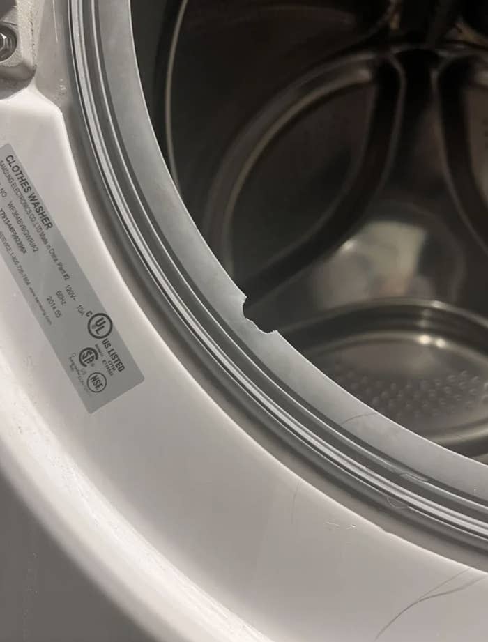 A close-up of a washing machine's open door, focusing on a torn rubber seal