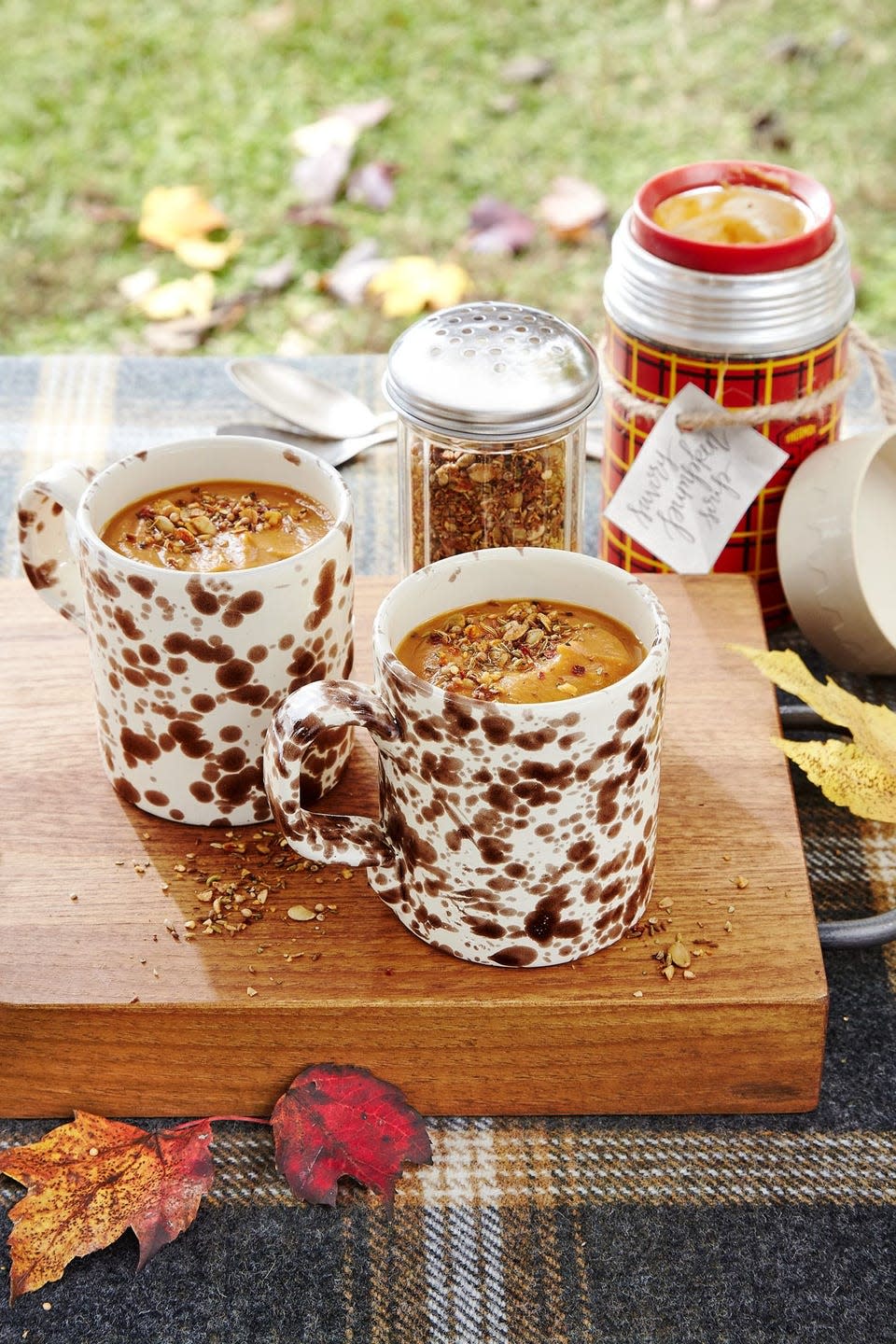 savory pumpkin soup in two brown and white mugs with spice shake on top