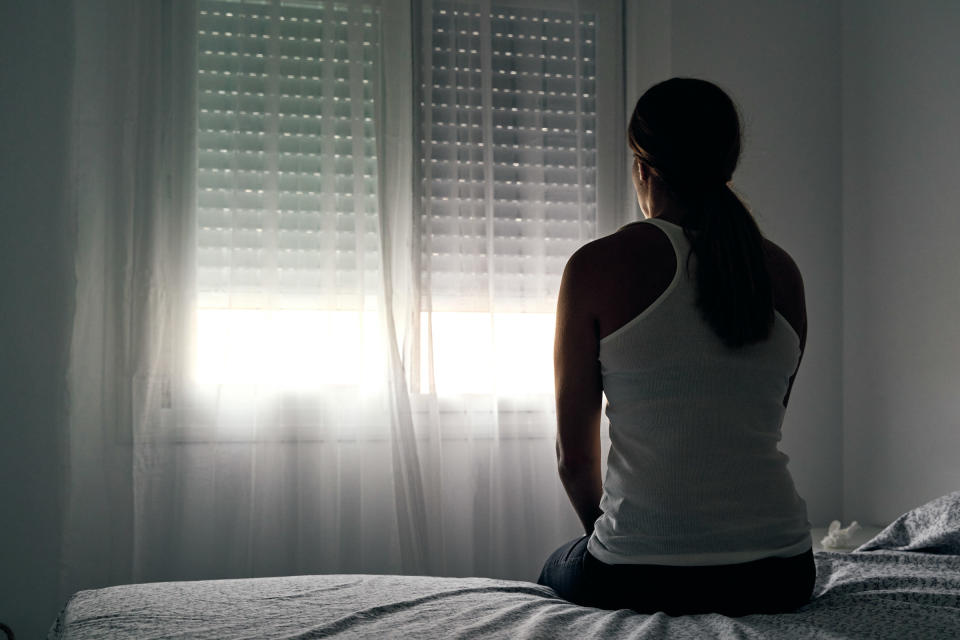 a woman sitting at the edge of the bed, her back toward the camera