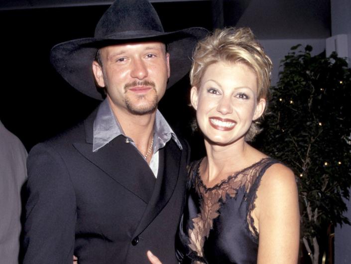 Tim McGraw in a black blazer and a black cowboy hat and Faith Hill in a black dress with her arms around McGraw