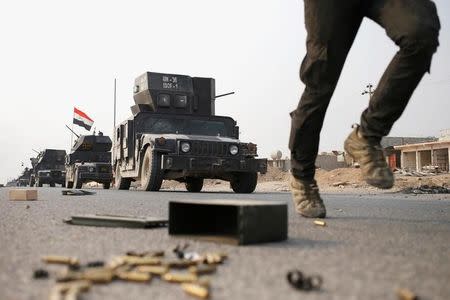 An Iraqi special forces soldier runs as other drive in armoured vehicles on a road near Mosul, Iraq October 25. 2016. REUTERS/Goran Tomasevic