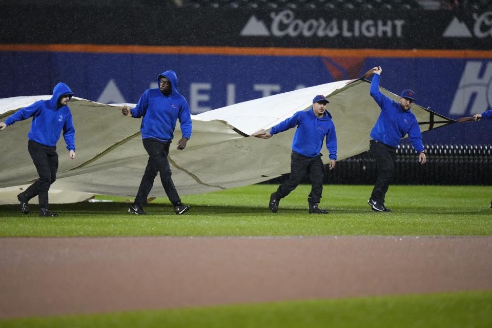 Grounds crew members cover the field during a rain delay in a baseball game between the New York Mets and the Miami Marlins early Friday, Sept. 29, 2023, in New York. The game was suspended. (AP Photo/Frank Franklin II)