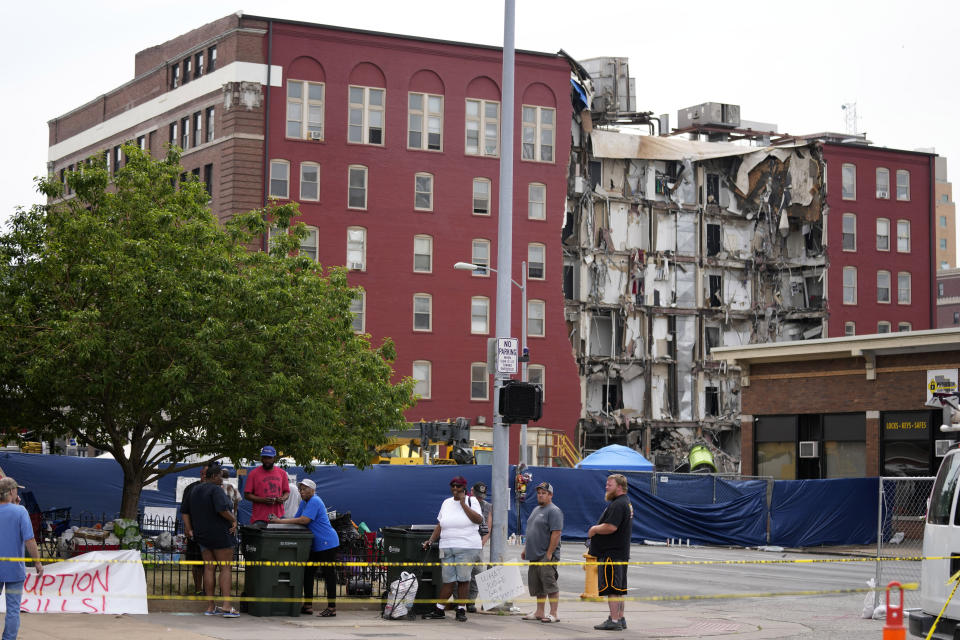 Local residents stand on a sidewalk near a collapsed apartment building, Monday, June 5, 2023, in Davenport, Iowa. The six-story, 80-unit building partially collapsed May 28. (AP Photo/Charlie Neibergall)